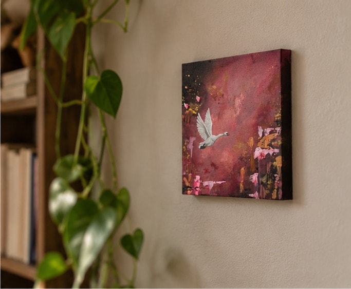 Flying Swan aan een lichte muur, van opzij gezien, naast een boekenkast en een hangende groene plant.