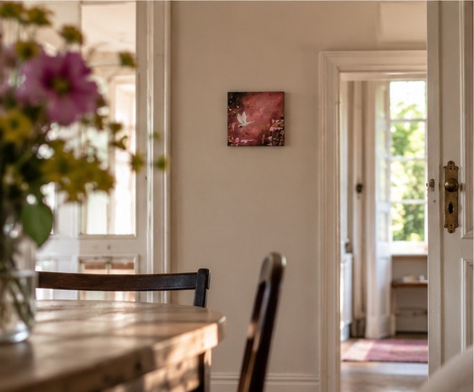 Flying Swan aan een lichte muur naast een openstaande witte deur, gezien langs een eettafel met een vaas bloemen.