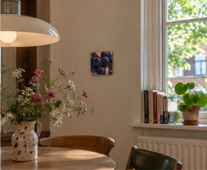 Blueberries aan de muur van een zonnige eethoek, met een gespikkelde kan met veldbloemen op tafel, een hanglamp en boeken in de vensterbank.
