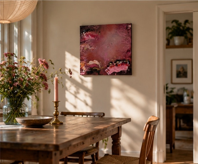 Gewichtloze Vleugels aan de muur van een eetkamer, boven een houten tafel met veldbloemen en een roze kaars, naast een openstaande deur.