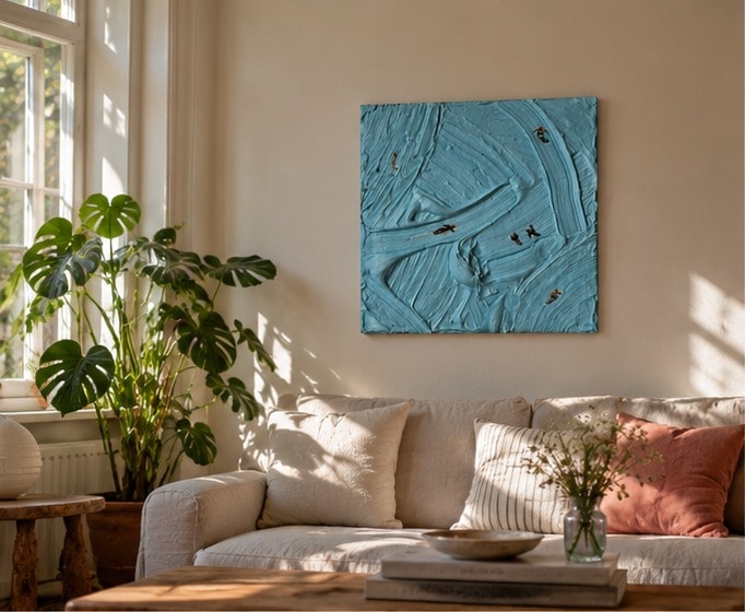 Catching Waves boven een linnen bank met crème, gestreepte en terracotta kussens in een zonnige woonkamer, naast een grote monstera bij het raam.