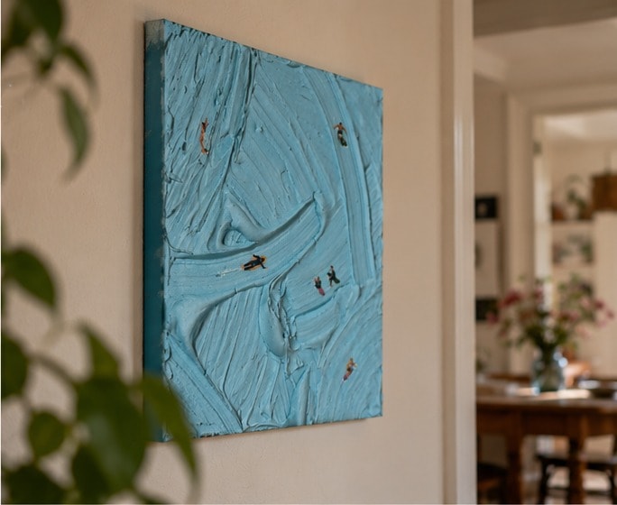 Catching Waves aan een lichte muur van opzij gezien, met de dikke verf en de donkerblauwe zijkant, en een doorkijk naar een eetkamer.